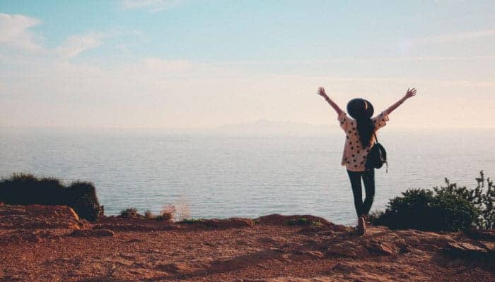 woman with hands raised looking out over ocean