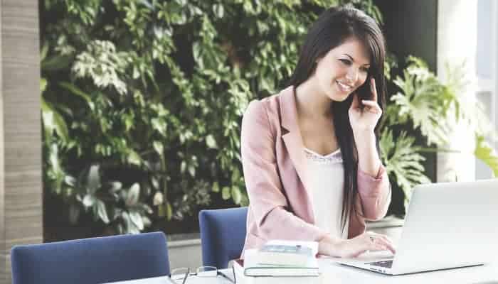 women with long brown hair and pink blazer sitting at table on the phone