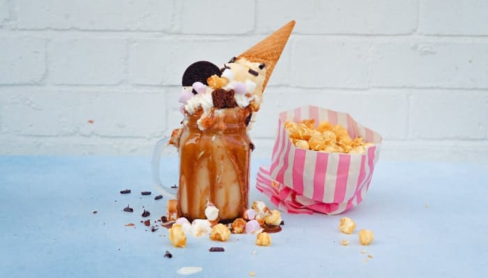 Jar overflowing with caramel, Oreos, ice cream, marshmallows, and chocolate bits next to pink striped bag of popcorn