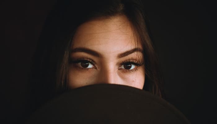 Closeup of a brunette woman hiding her mouth with a brown hat because she is worried about her chronic bad breath