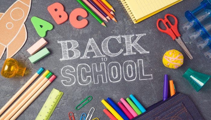 Aerial view of a black chalkboard surrounded by school supplies with Back to School written in the middle