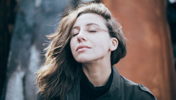 Brunette woman practices relaxation techniques as she takes deep breaths with her eyes closed