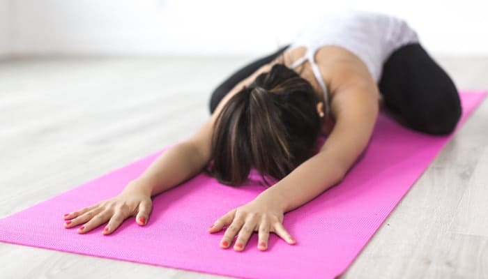 Brunette woman wears exercise clothes and lies in Child's Pose on a pink yoga mat