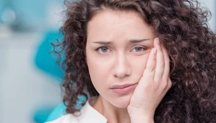 Curly-haired woman touches her cheek due to tooth pain because she needs root canal therapy