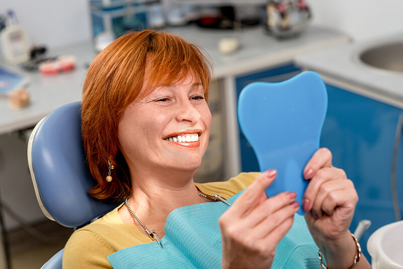 woman examining her smile in a mirror